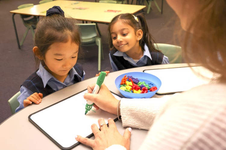 Two children working at a desk learning with a teacher